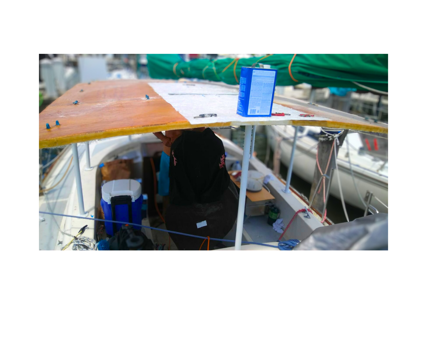 "Sailboat under repair with a partially installed wooden deck, tools, and repair materials visible at a marina."