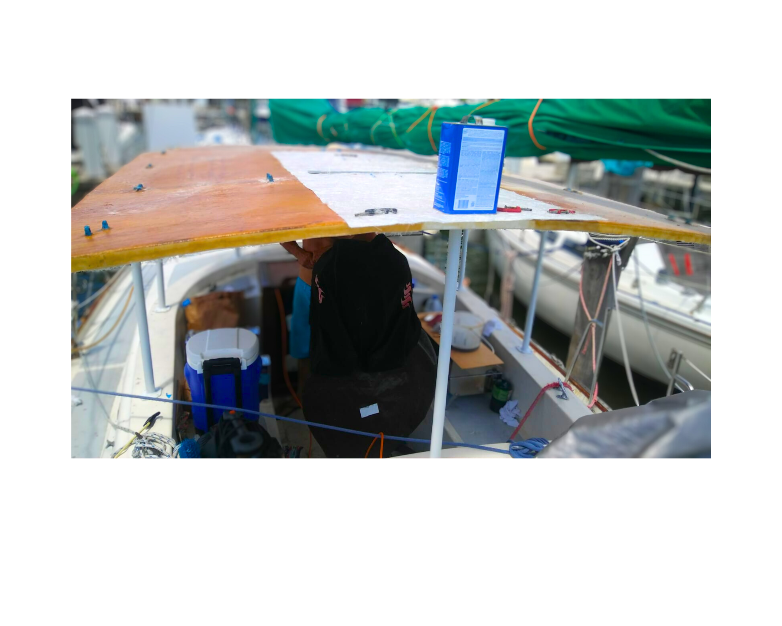 "Sailboat under repair with a partially installed wooden deck, tools, and repair materials visible at a marina."