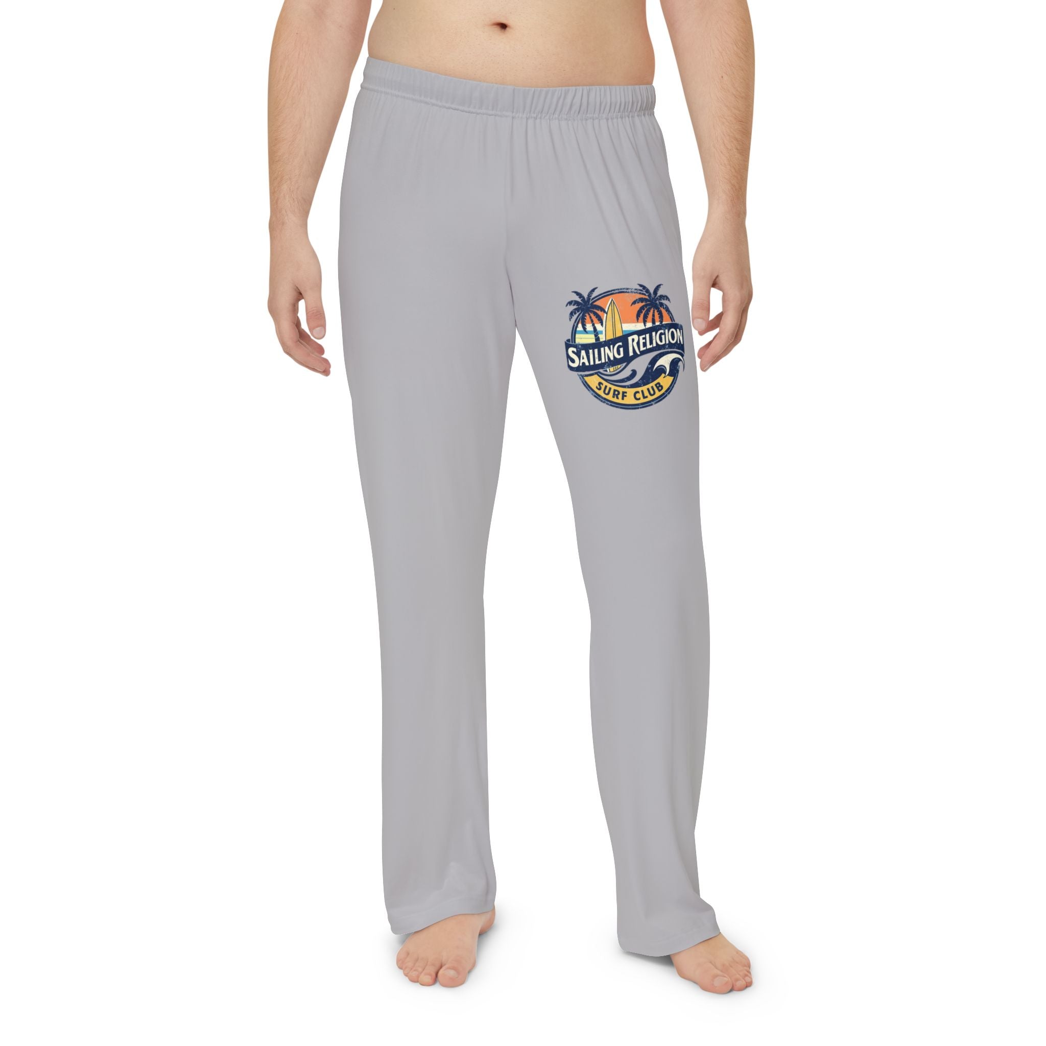 Man wearing light gray Sailing Religion men’s pajama pants featuring a retro surf club logo with palm trees and sunset — soft, coastal-inspired lounge pants designed for comfort and ocean lifestyle.