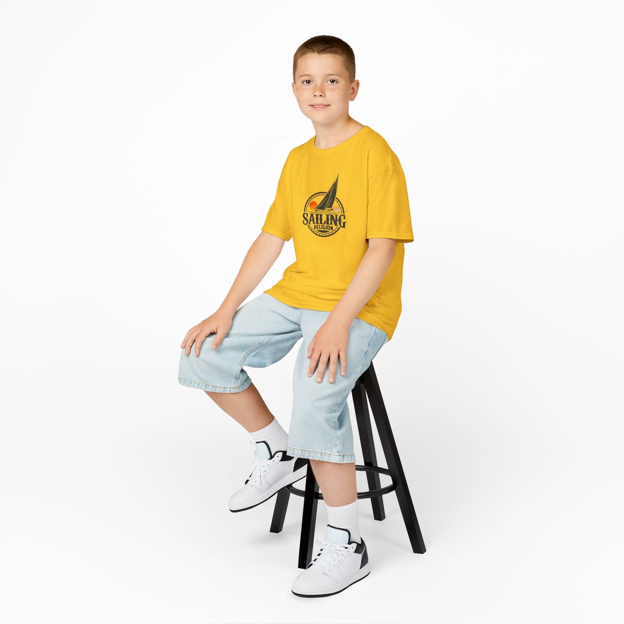 Boy wearing a yellow Sailing Religion kids’ t-shirt featuring a sailboat graphic logo — ocean-inspired children’s shirt designed for comfort, movement, and coastal adventure.